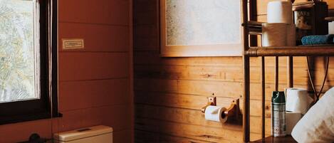 A wooden-paneled bathroom with a toilet, a shelf with toiletries, and a framed picture on the wall.
