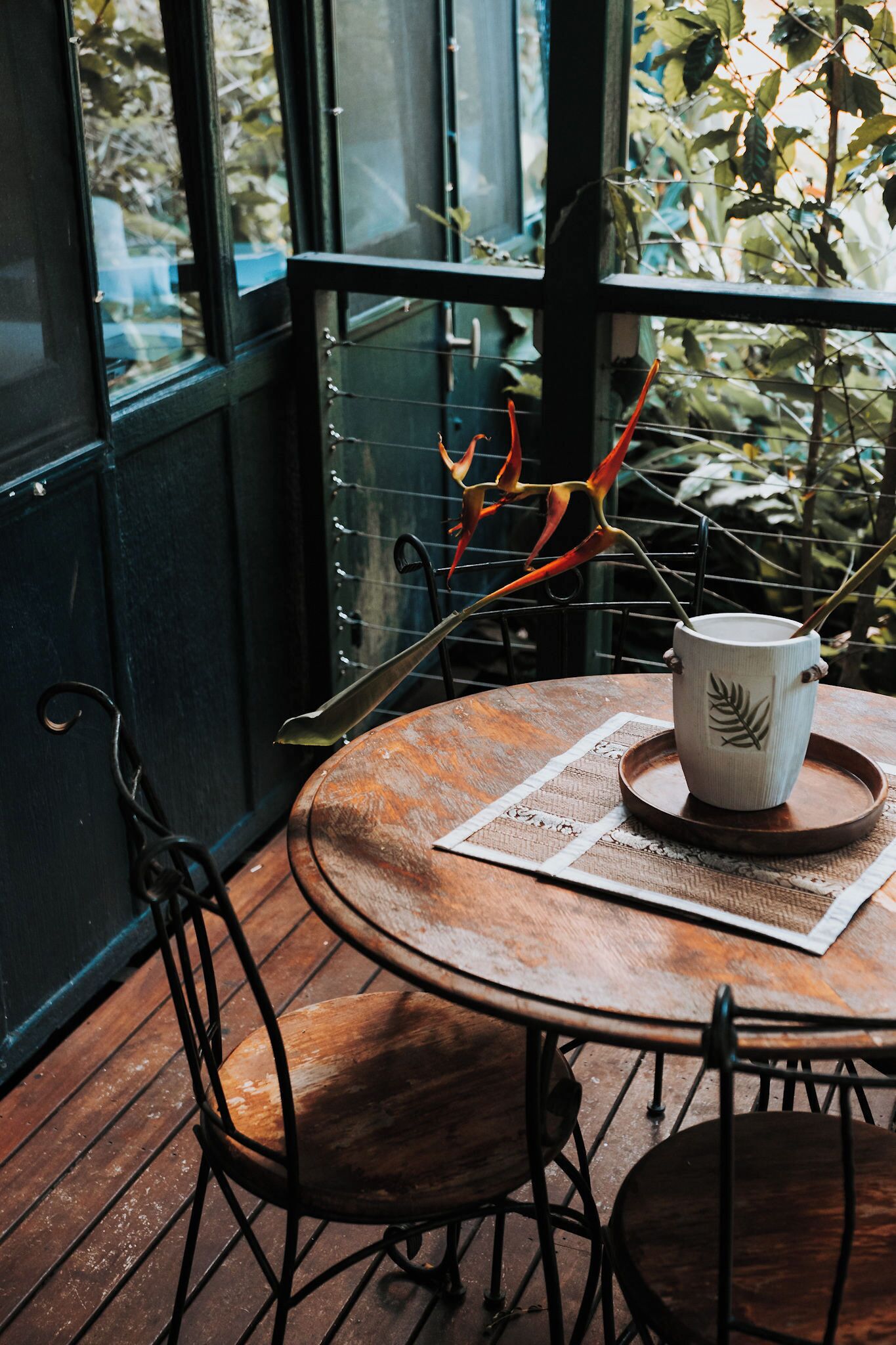 A round wooden table with a white ceramic mug and a decorative leaf pattern, surrounded by metal chairs.