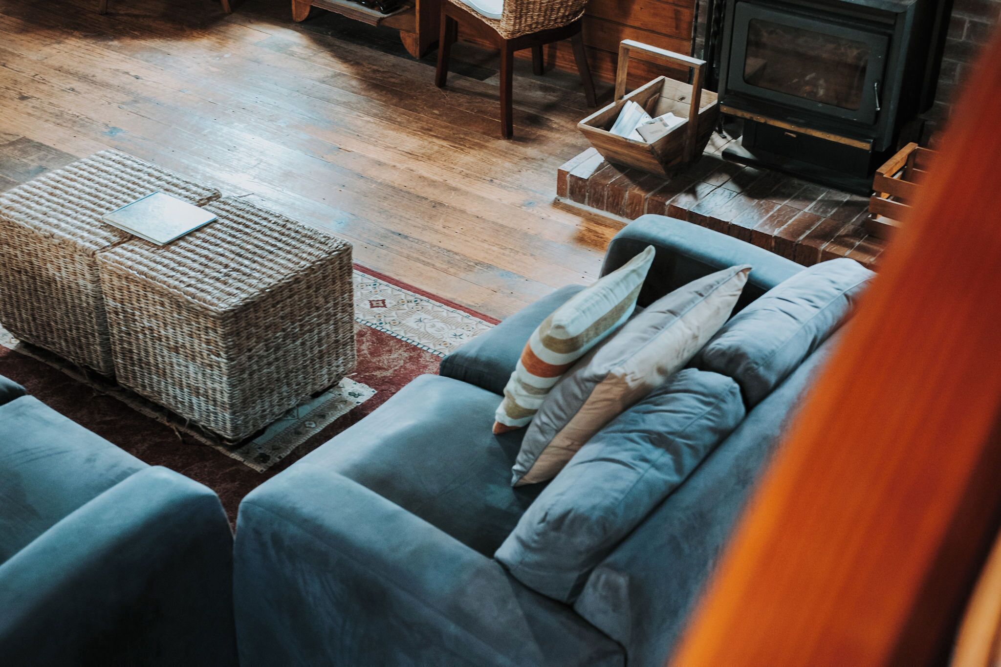 A cozy living room with a sofa, wicker ottoman, and a fireplace.