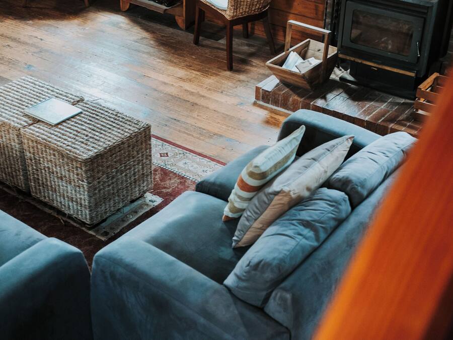 A cozy living room with a sofa, wicker ottoman, and a fireplace.