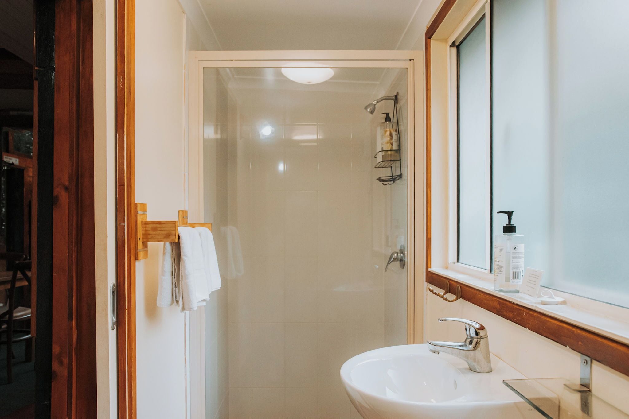 A bathroom with a glass shower enclosure, a white sink, and a mirror with a wooden frame.