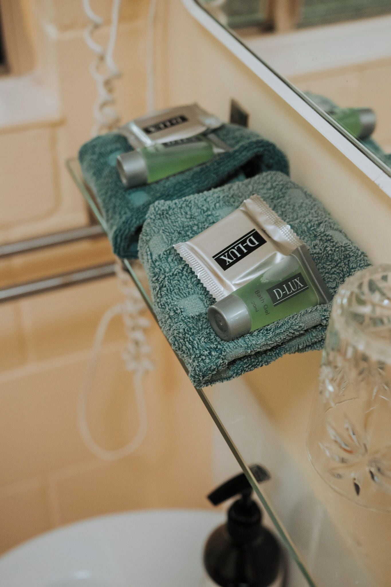 Een badkamer met een handdoekhouder, waarop een groene handdoek en een tube D-Lux badgel liggen.