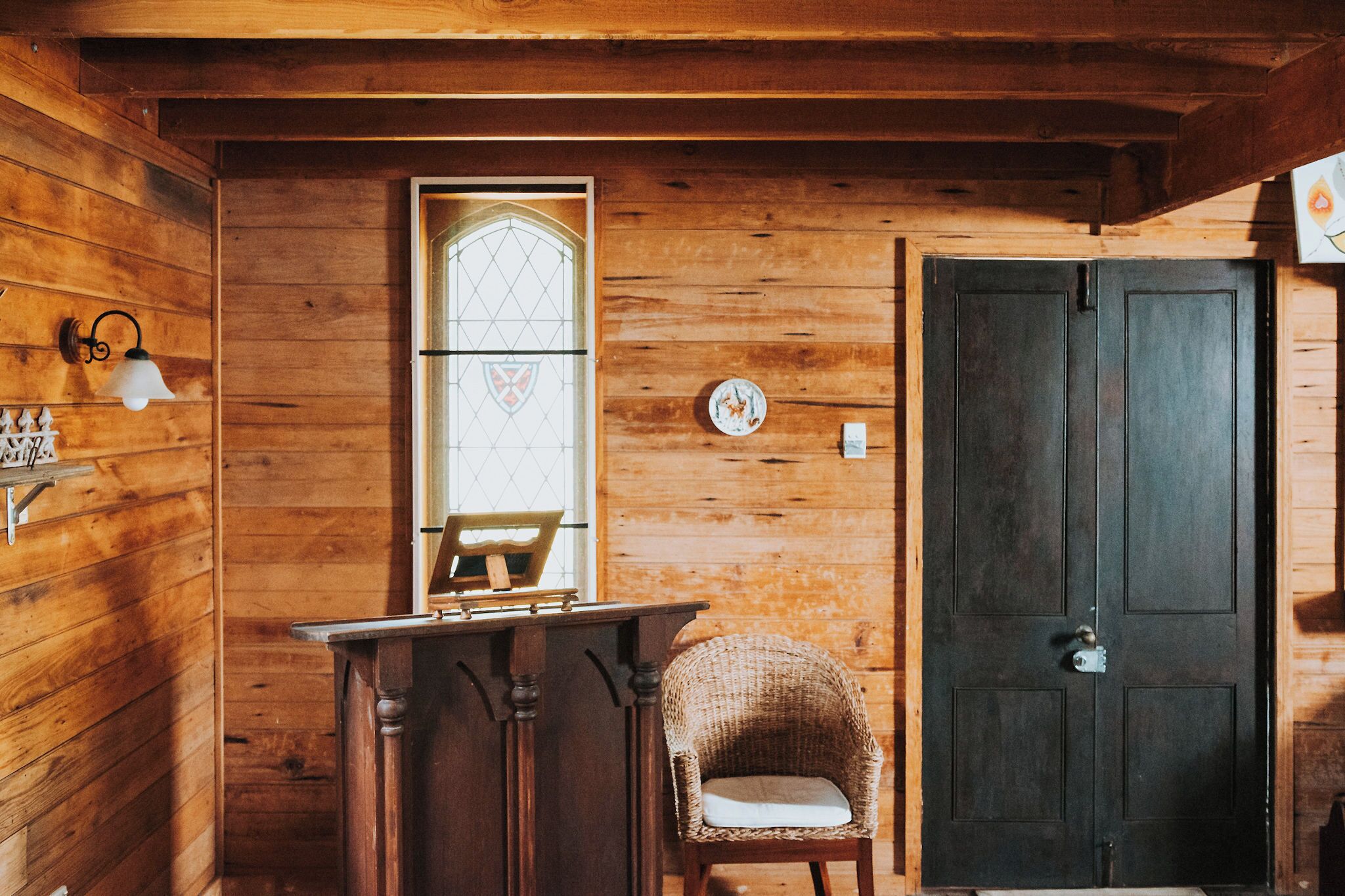 Un interior de madera con una puerta, una ventana con un diseño de vitral, una silla y una pequeña mesa.