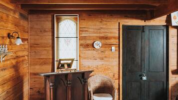 Un interior de madera con una puerta, una ventana con un diseño de vitral, una silla y una pequeña mesa.