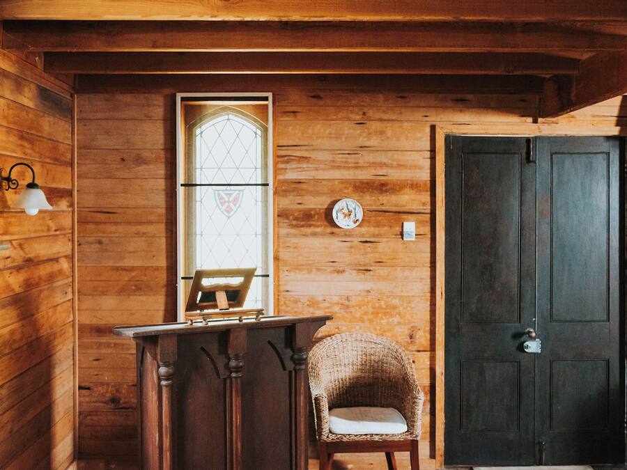 Un interior de madera con una puerta, una ventana con un diseño de vitral, una silla y una pequeña mesa.