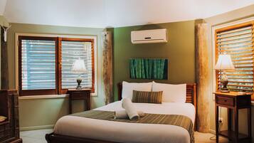 Een hotelkamer met een bed, twee nachtkastjes, een wandairconditioner en een raam met jaloezieën.