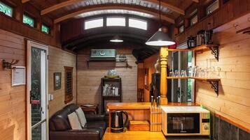 L’intérieur chaleureux d’un chalet avec un plafond en bois, une table à manger, un canapé, un coin cuisine et une fenêtre offrant une belle vue.
