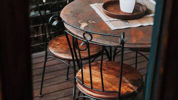 Une table ronde en bois, des chaises en métal, un vase blanc avec une plante et, au fond, une rambarde en métal.