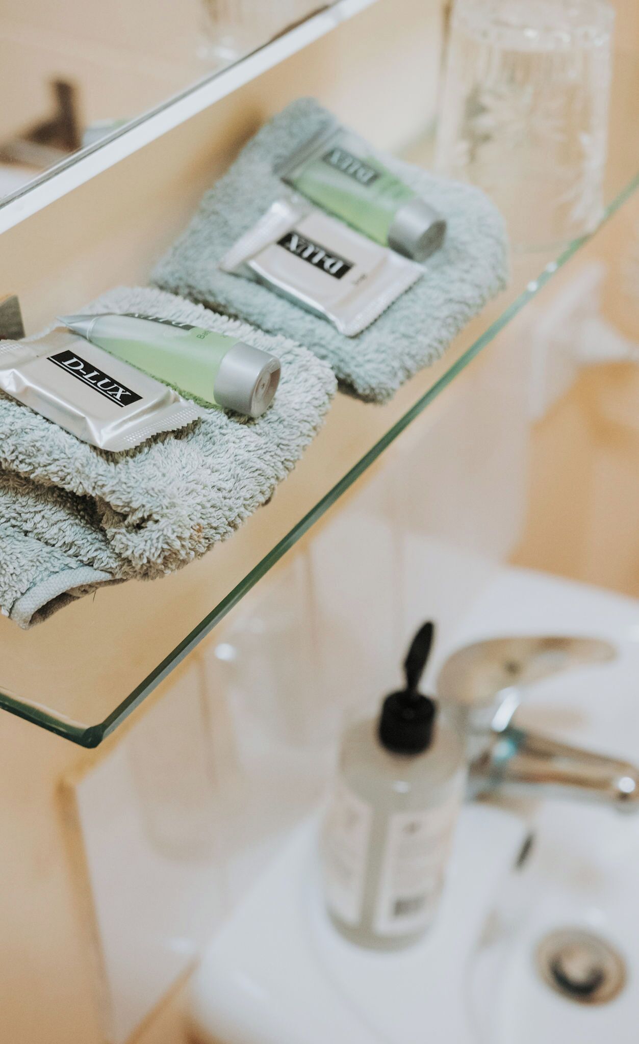 A bathroom with a glass shelf holding toiletries, a towel, and a bottle of hand sanitizer.
