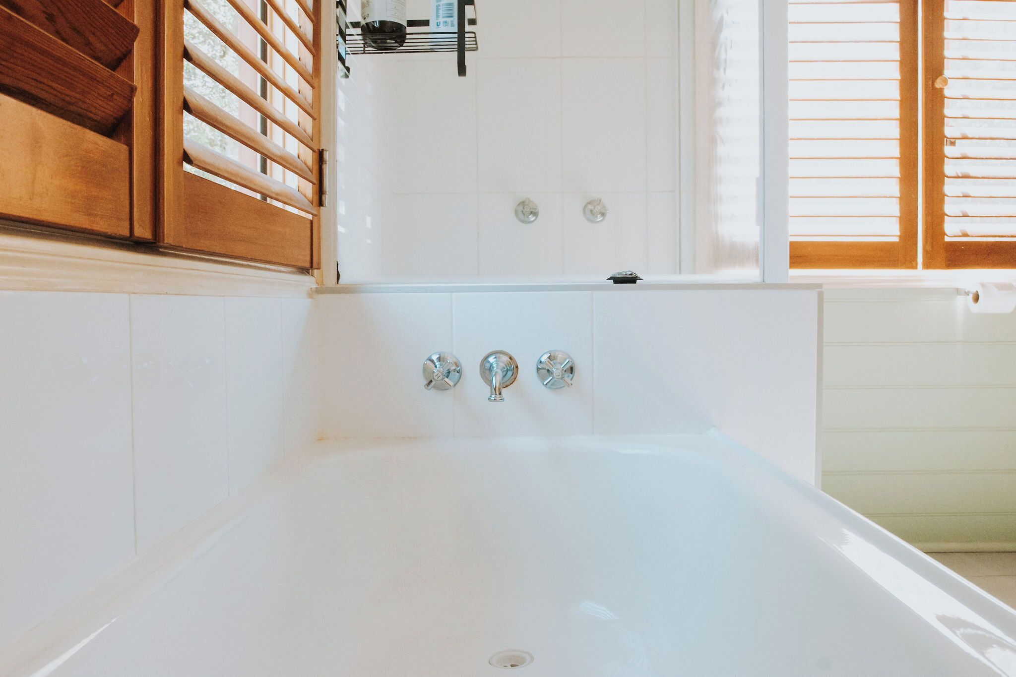 Une salle de bain avec une baignoire blanche, des meubles en bois et une fenêtre avec des stores.