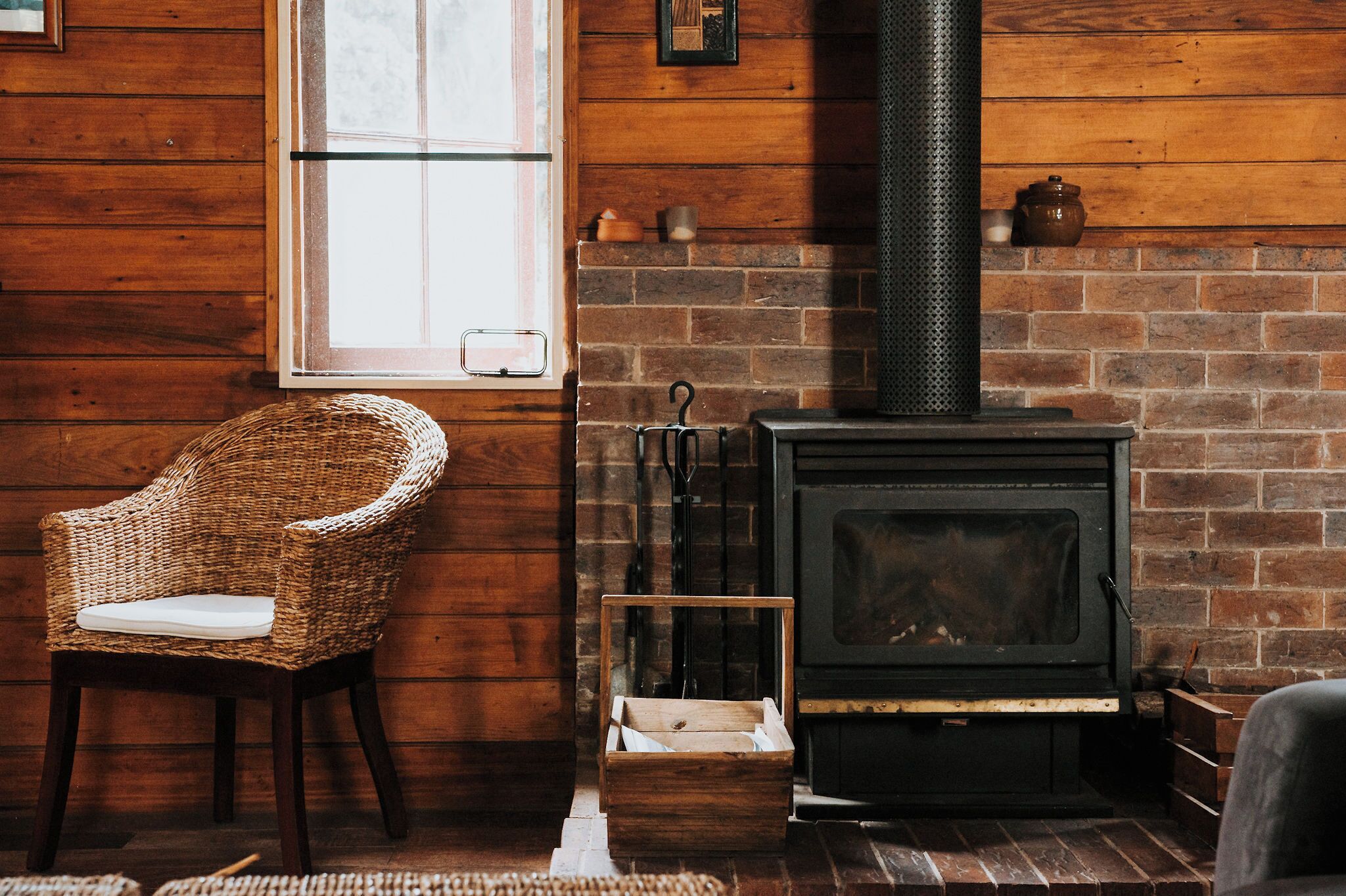 A rustic room with a brick fireplace, a wicker chair, and a wooden bench.