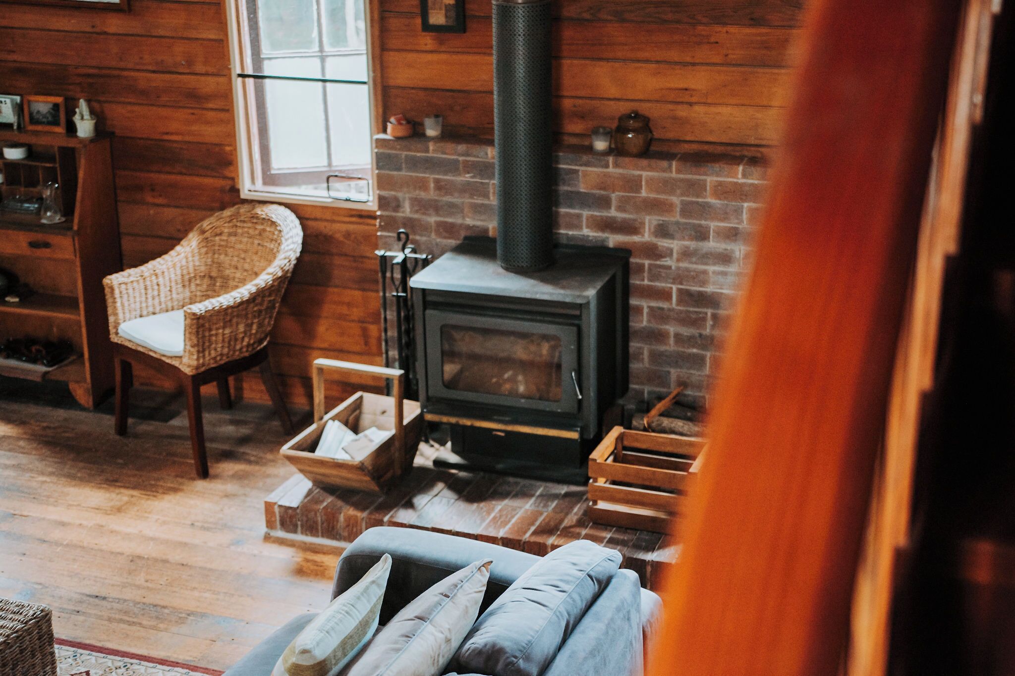 Una habitación acogedora con chimenea de ladrillo, una silla de mimbre y un sofá con cojines.