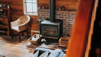 Una habitación acogedora con chimenea de ladrillo, una silla de mimbre y un sofá con cojines.