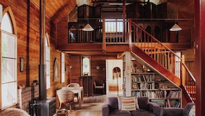 Een ruime loft met hoge plafonds, zichtbare houten balken, een trap en een grote boekenkast.