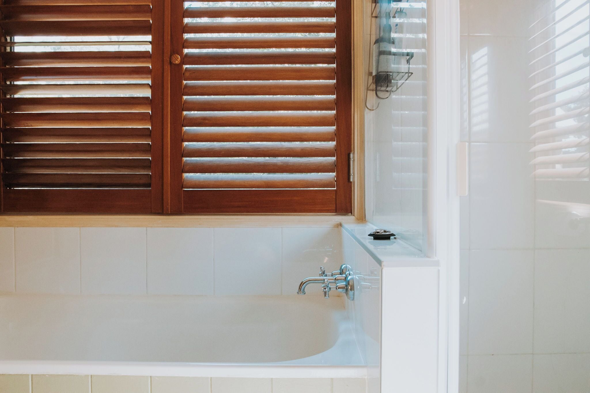 Une salle de bain avec une baignoire, des stores en bois et un mur recouvert de carreaux.