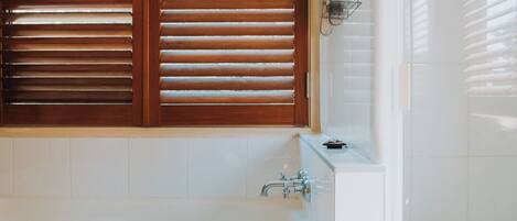Une salle de bain avec une baignoire, des stores en bois et un mur recouvert de carreaux.