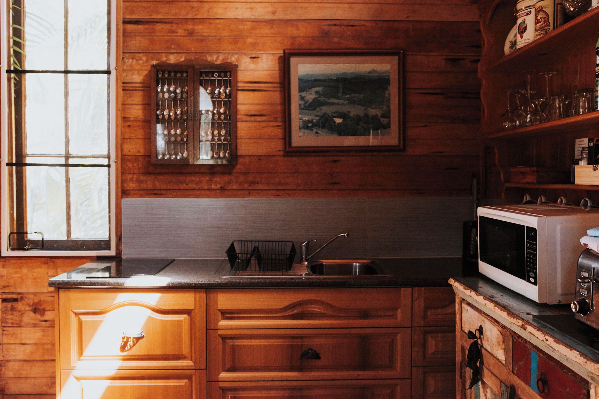 A kitchen with wooden cabinets, a sink, a microwave, and a window with blinds.