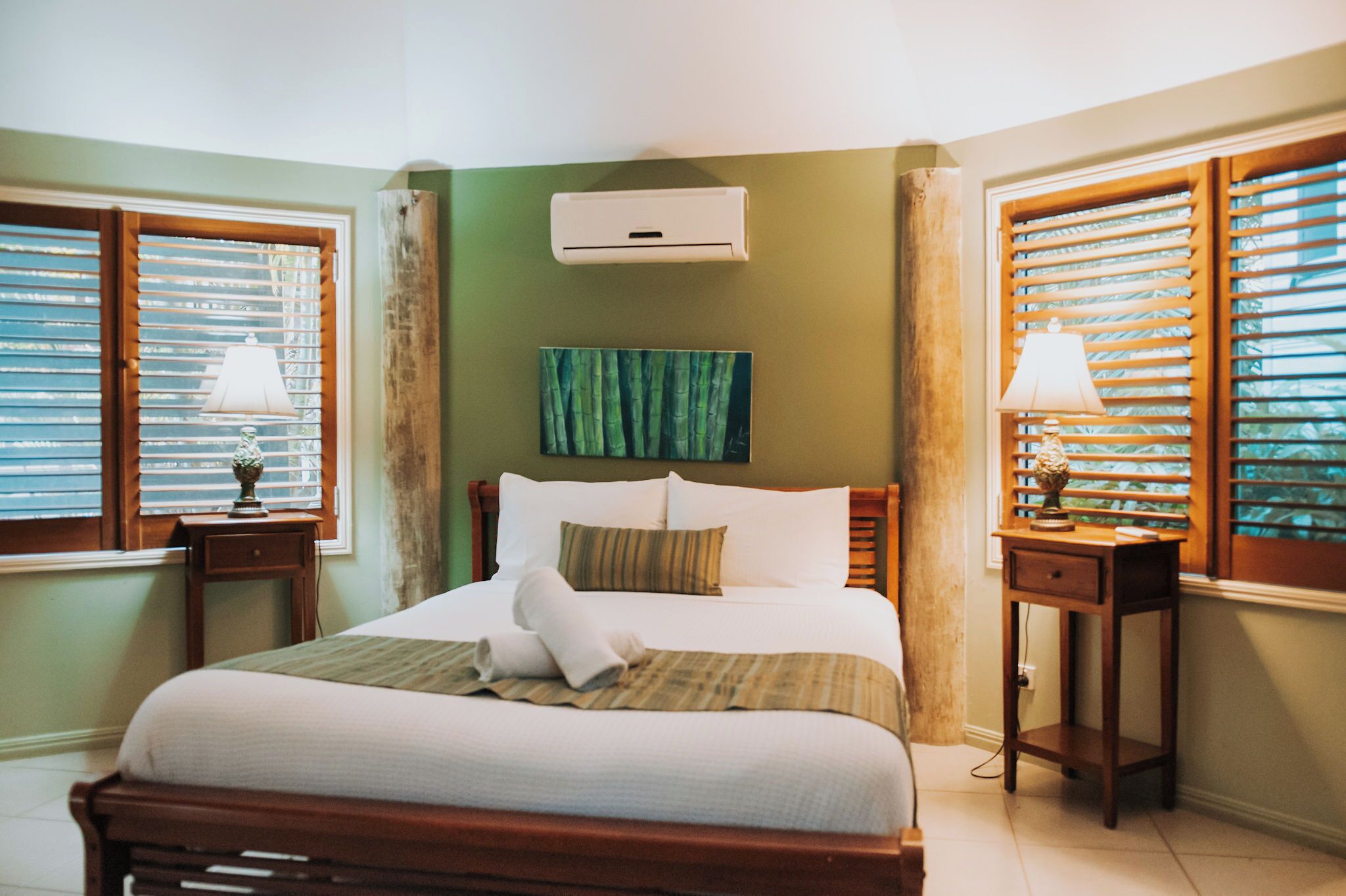 A neatly made bed with a pillow, a bedside lamp, and a wall-mounted air conditioner.