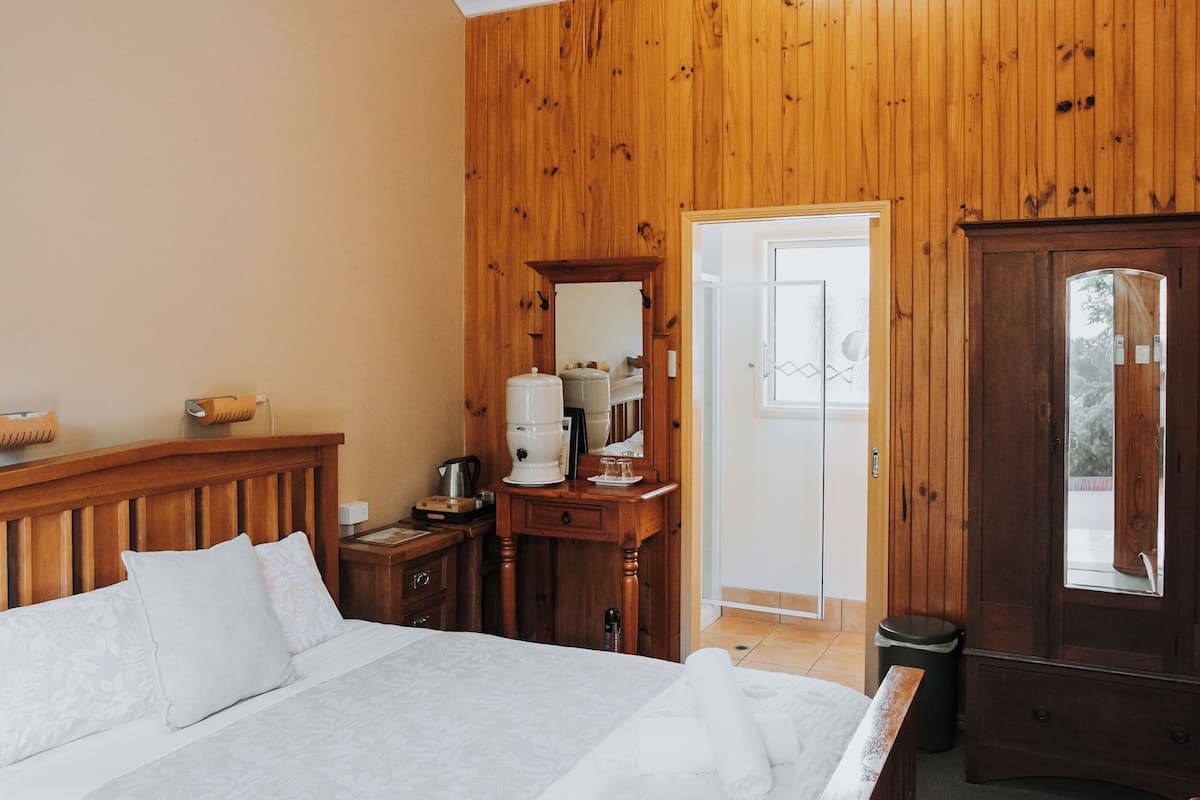 Une pièce aux murs lambrissés, comprenant un lit, une commode en bois, un miroir, une machine à café et une poubelle.