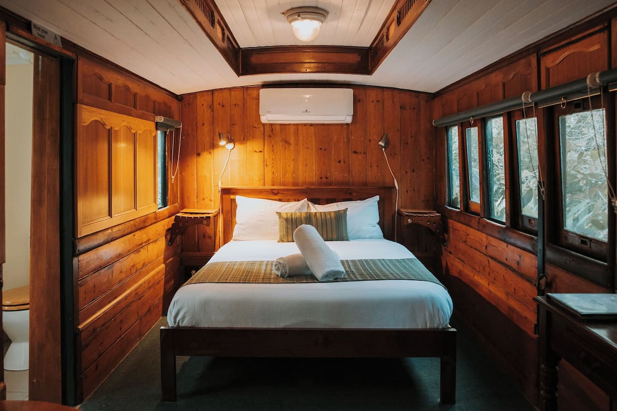 Une chambre de style cabane en bois, avec un lit, des lampes de chevet, un appareil de climatisation et des fenêtres.