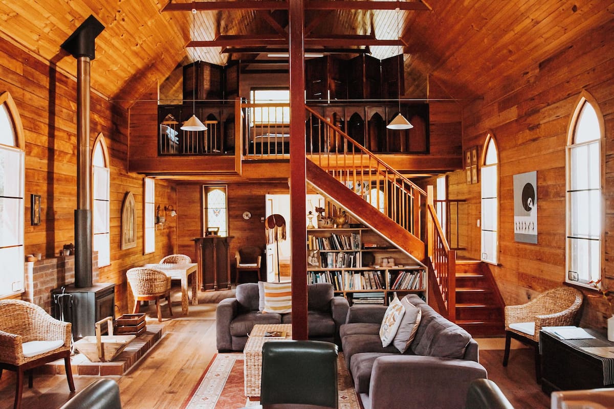 Un intérieur spacieux en bois, avec un escalier, un coin salon et des étagères à livres.
