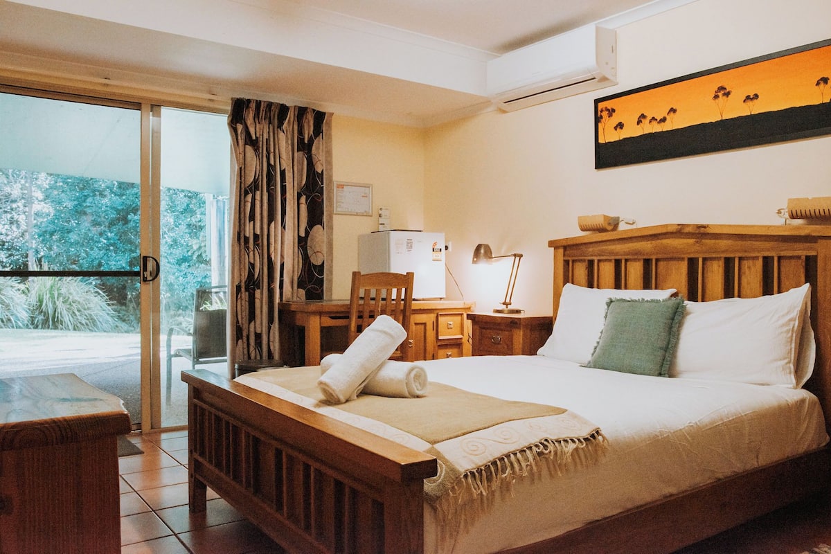 Une chambre à coucher avec un lit, un bureau, une chaise, une fenêtre avec des rideaux et un tableau au mur.