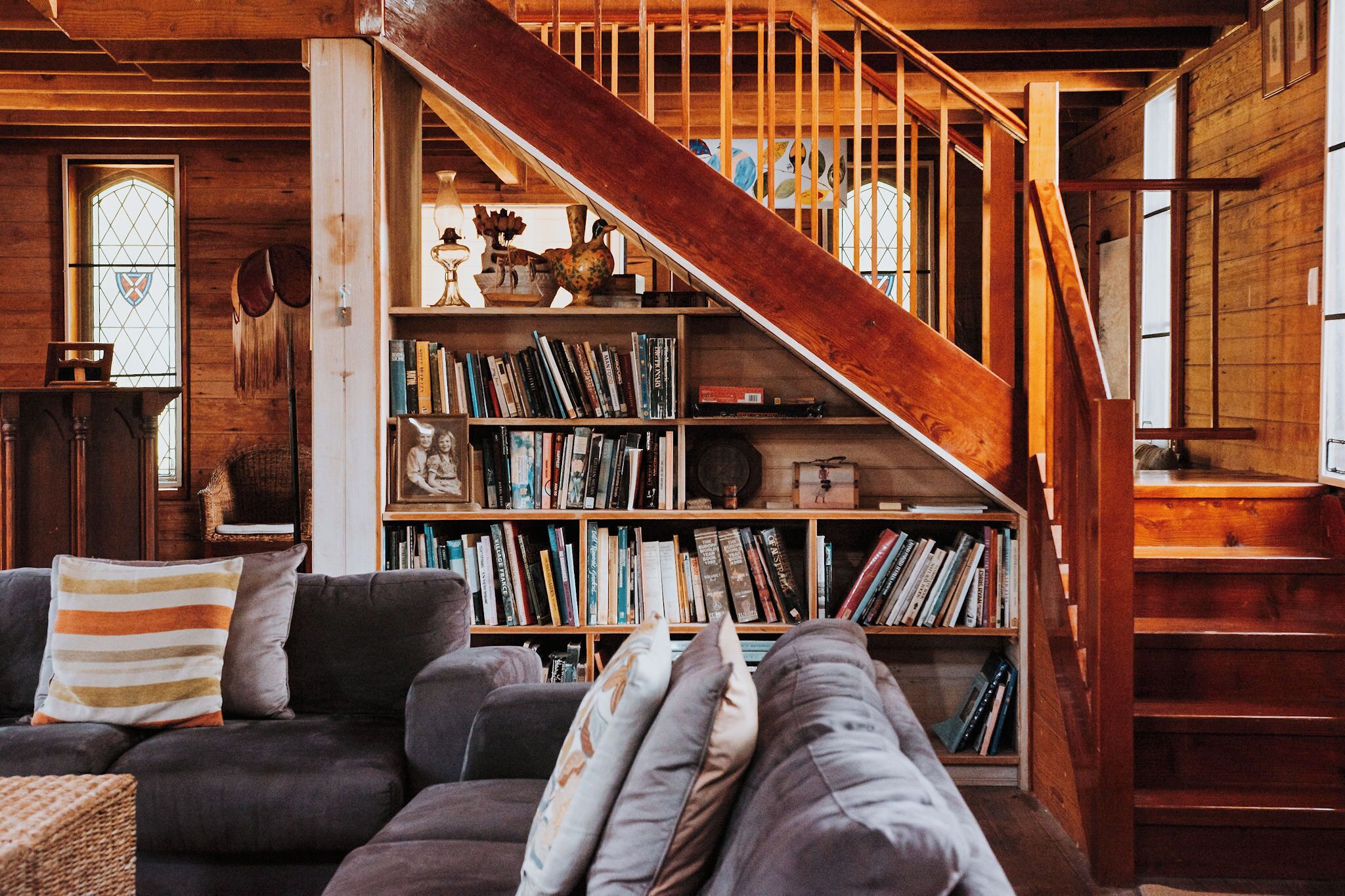 Een gezellige woonkamer met een trap, een boekenplank vol boeken en een glas-in-loodraam.