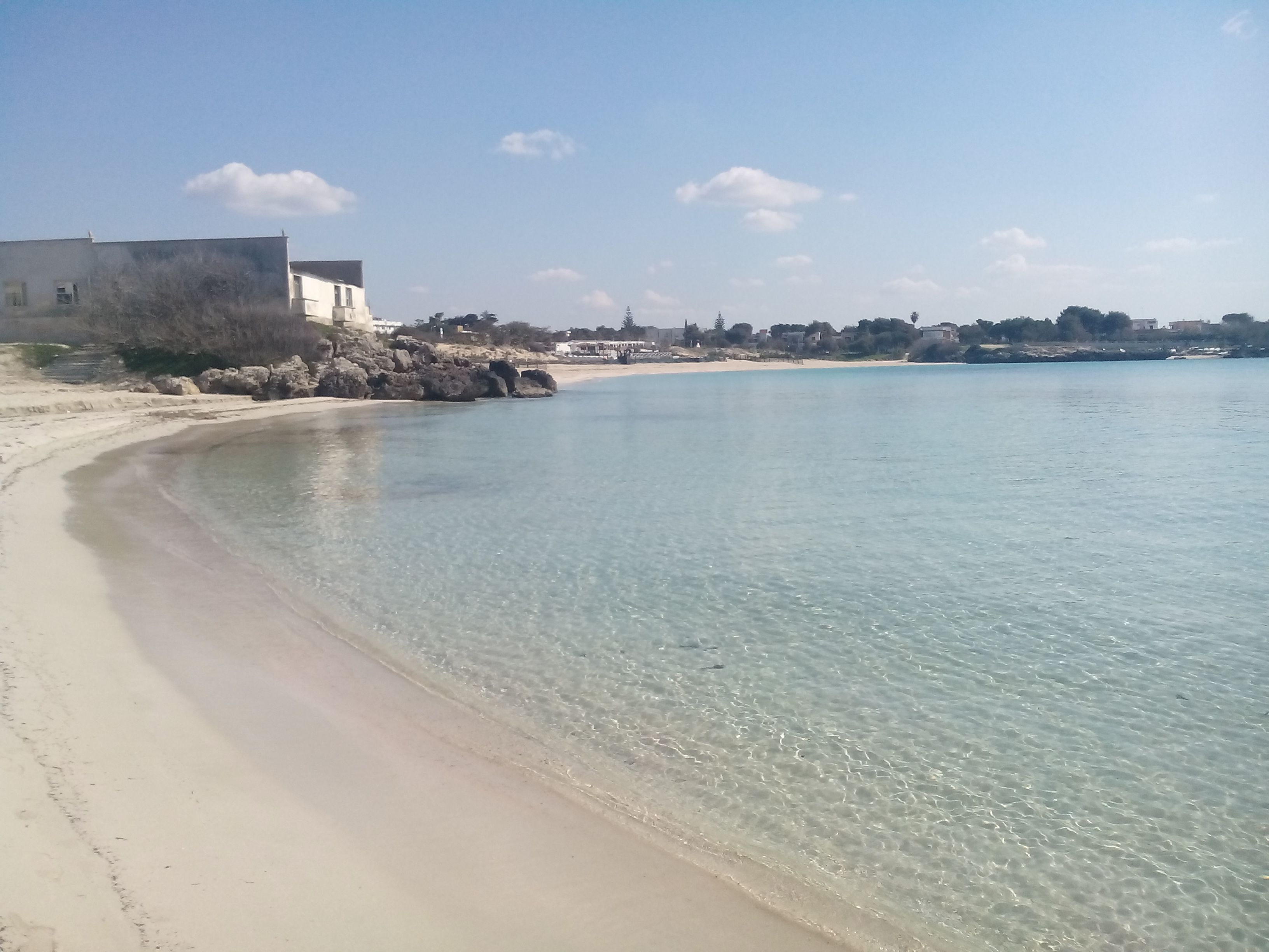Una playa con aguas cristalinas, una orilla arenosa y un edificio al fondo.