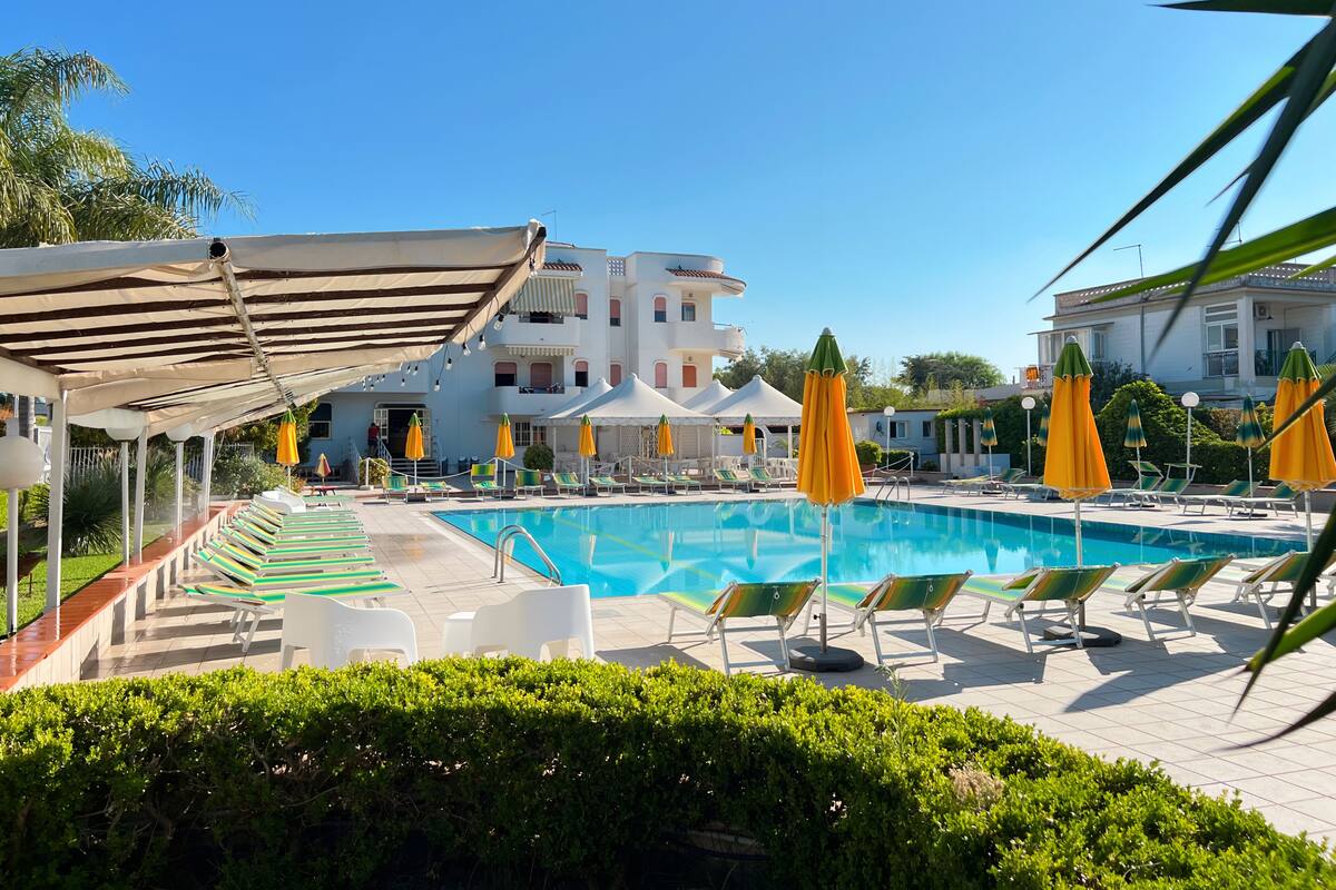 Ein Pool mit Liegestühlen und Sonnenschirmen, umgeben von Gebäuden.