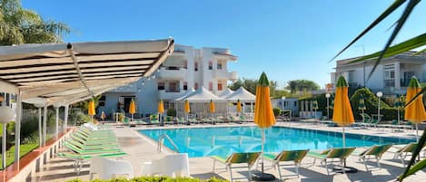A swimming pool with lounge chairs and umbrellas, surrounded by buildings.