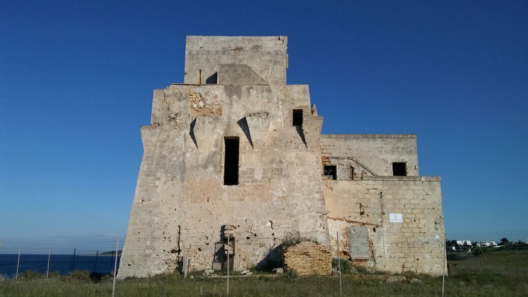 Une vaste structure en béton délabrée, dotée de nombreuses ouvertures et d’un toit plat, située près d’une étendue d’eau.