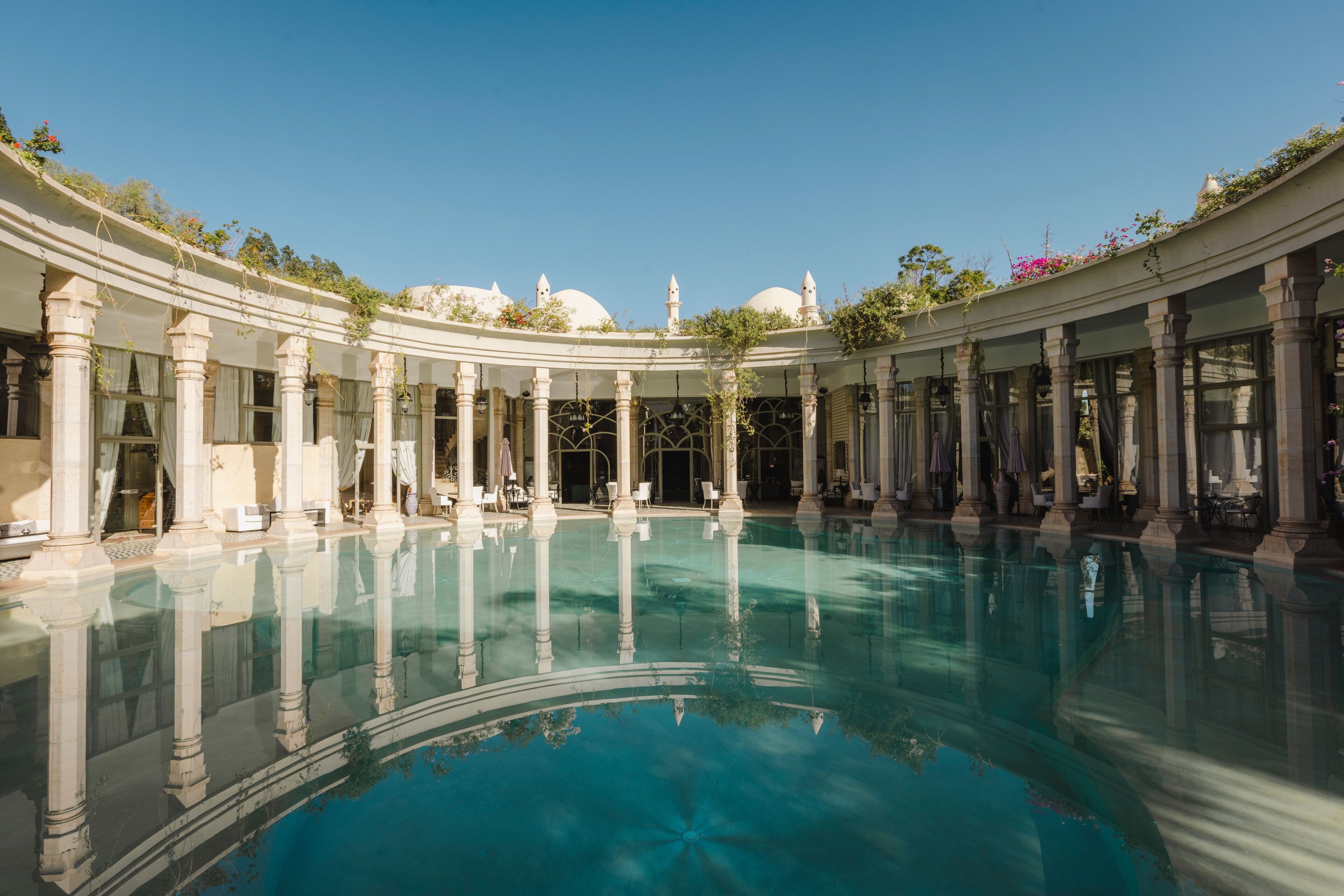 A large indoor swimming pool with classical architecture, including columns and arches, surrounded by seating areas.