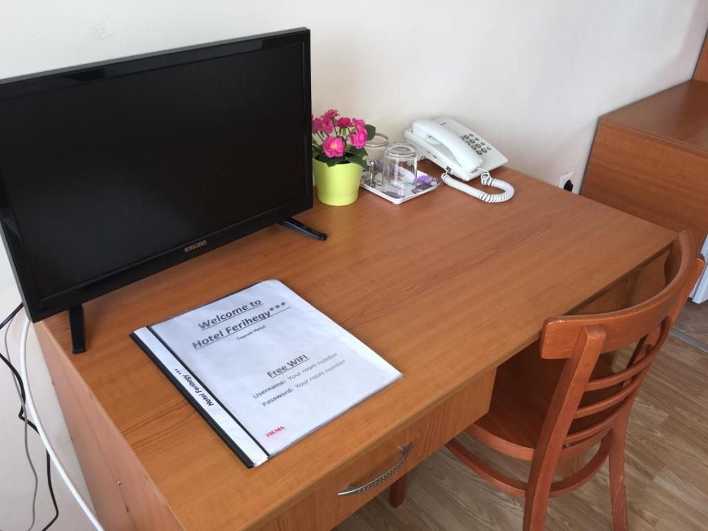 Un escritorio con un monitor de computadora, un folleto de bienvenida, un teléfono y una pequeña planta en maceta.