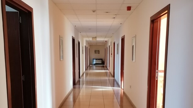 Un long couloir étroit, avec un sol carrelé et des portes de part et d’autre.