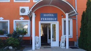 L’entrée d’un hôtel, avec une enseigne indiquant « HÔTEL FERIHEGY », un porche et deux statues de lions.