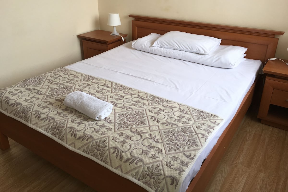 A neatly made bed with a patterned bedspread, white pillows, and a rolled white towel.