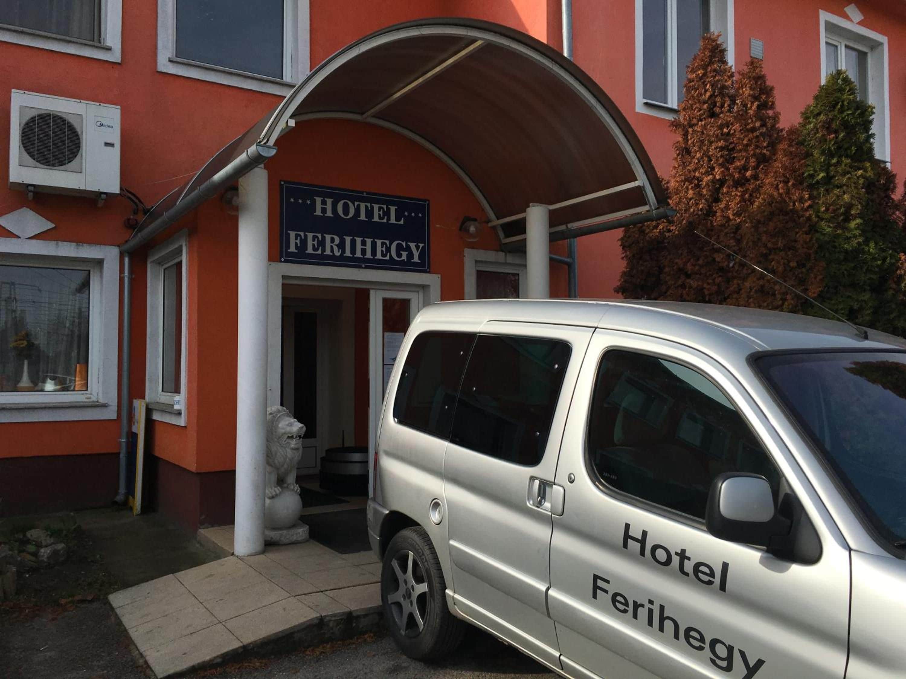 Una furgoneta plateada estacionada frente a un edificio con un letrero que dice 'Hotel Ferihegy'.