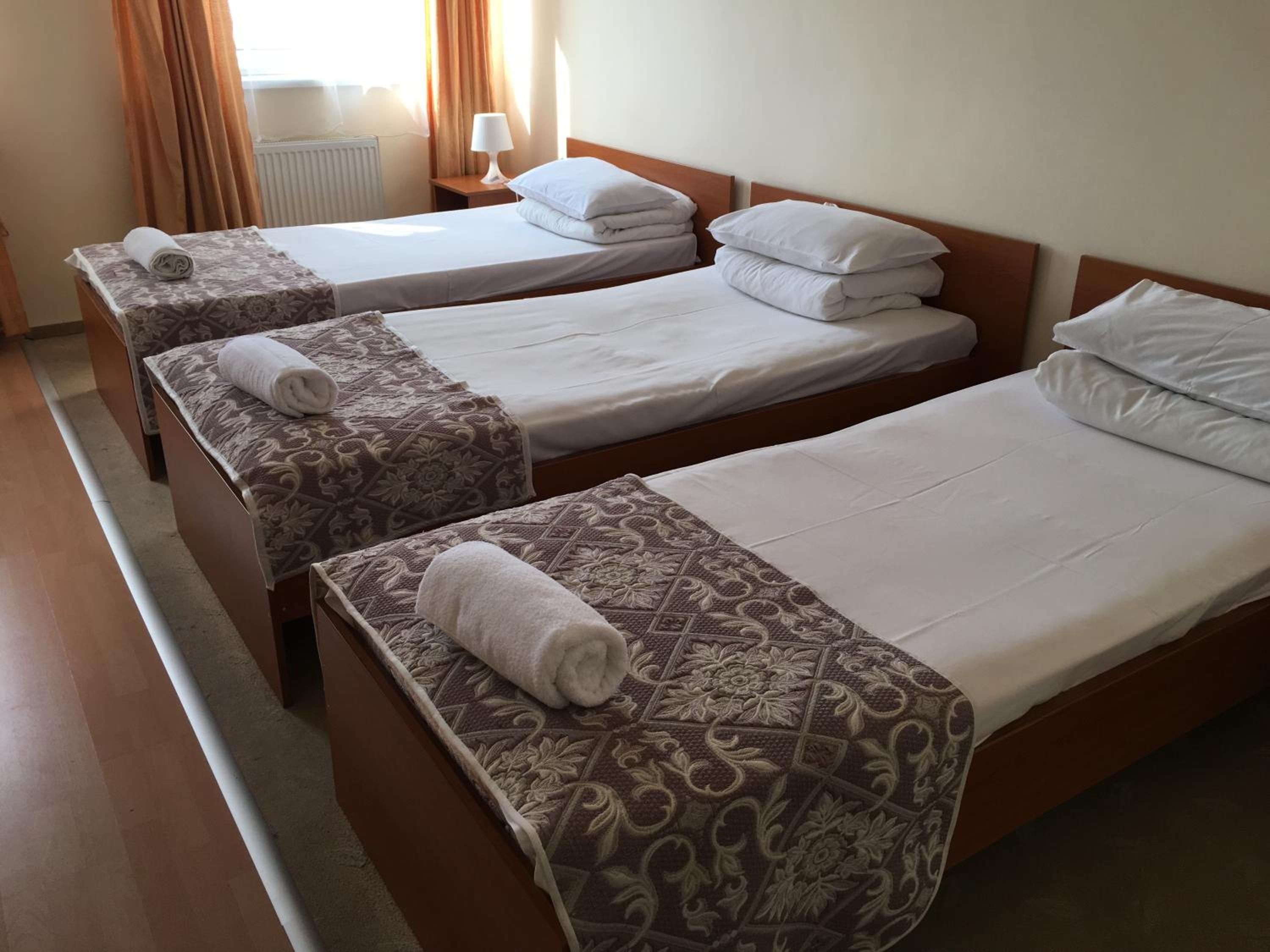 A hotel room with three single beds, each with a patterned bedspread and a rolled towel.