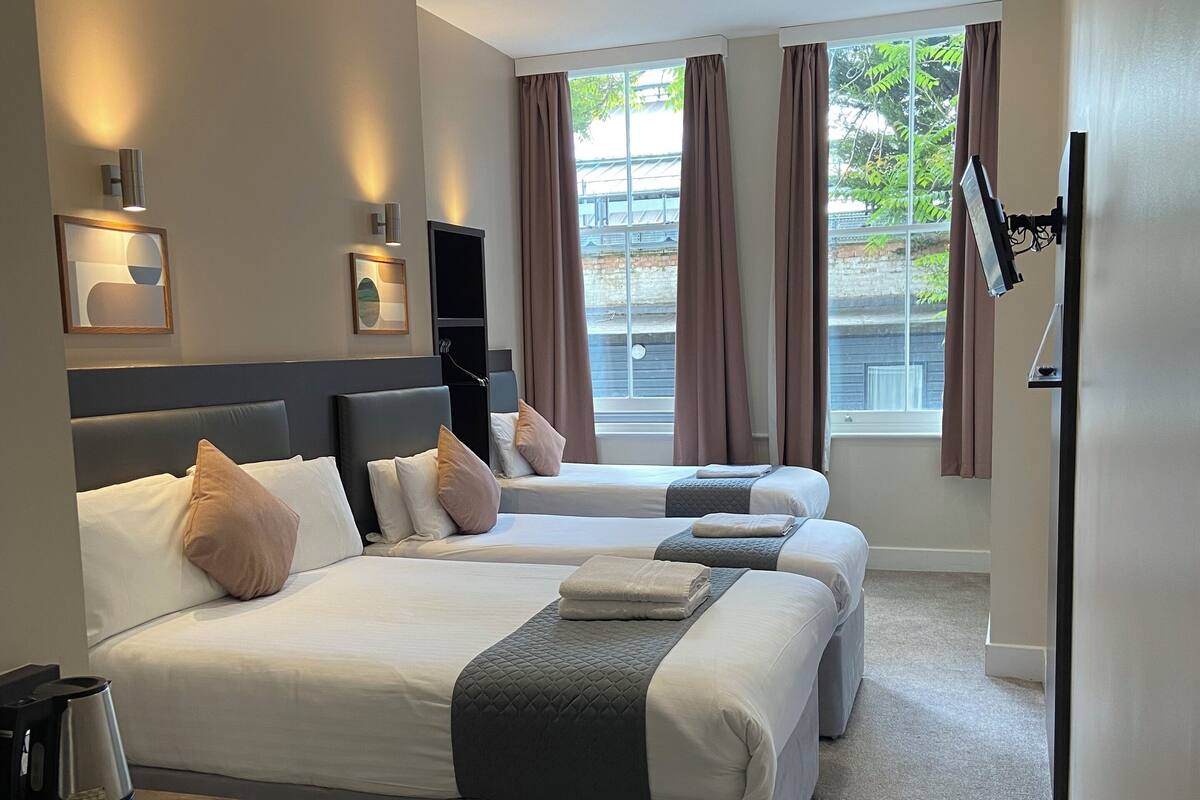 Une chambre d’hôtel avec deux lits, un téléviseur à écran plat fixé au mur et une fenêtre avec des rideaux.