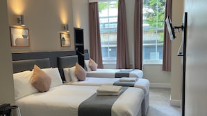 Ein Hotelzimmer mit zwei Betten, einem an der Wand befestigten Flachbildfernseher und einem Fenster mit Vorhängen.