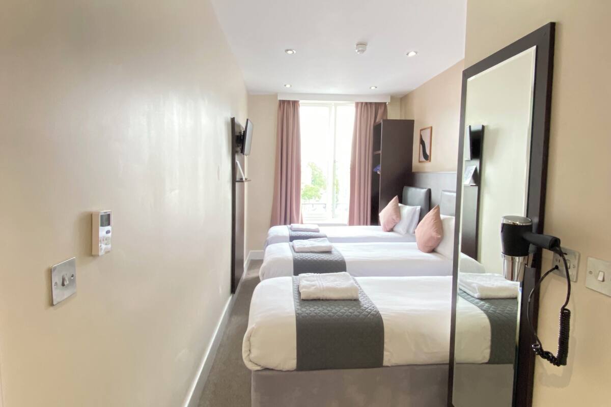Une chambre d’hôtel avec deux lits, un grand miroir, un sèche-cheveux et un panneau de commande au mur.