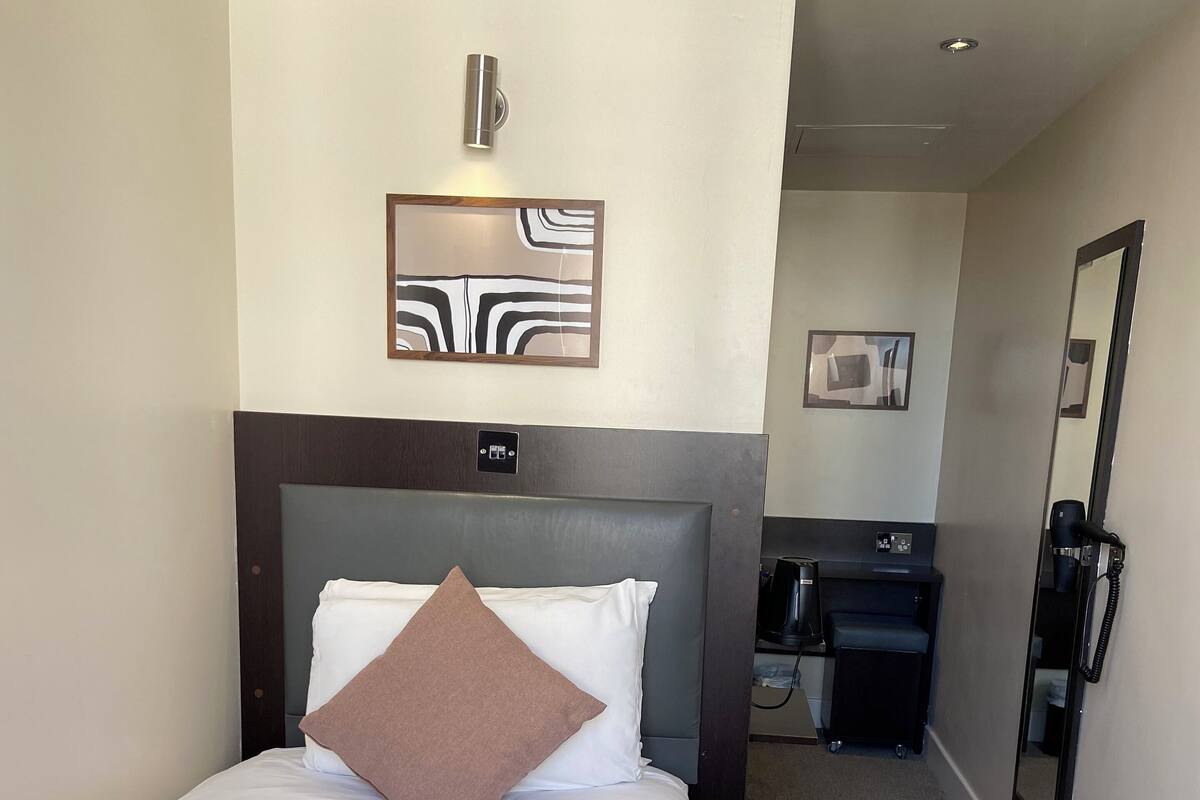 Une chambre d’hôtel comprenant un lit, une table de chevet, un miroir et un luminaire fixé au mur.
