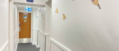 A hotel corridor with a sign indicating the direction to the lobby, a closed room door, and decorative wall stickers.
