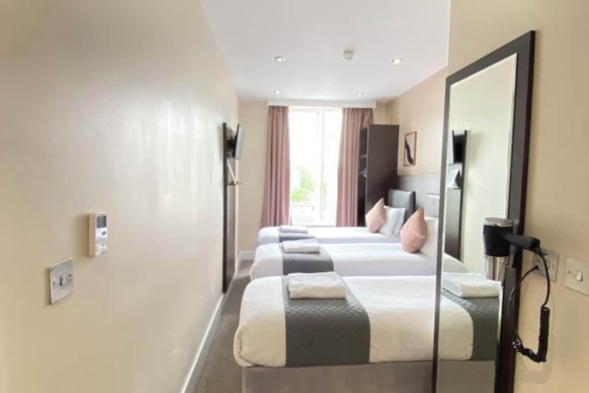A hotel room with two beds, a large mirror, a TV, and a window with curtains.