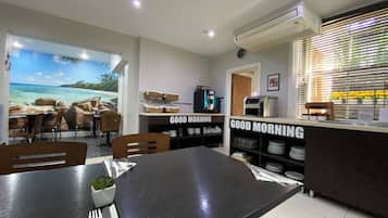 A modern dining area with a view of a beach through a large window. There is a counter with a 'Good Morning' sign and a coffee machine.