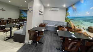 Ein Restaurant mit Tischen und Stühlen, einem Wandbild mit Strandmotiv und einer Klimaanlage an der Wand.