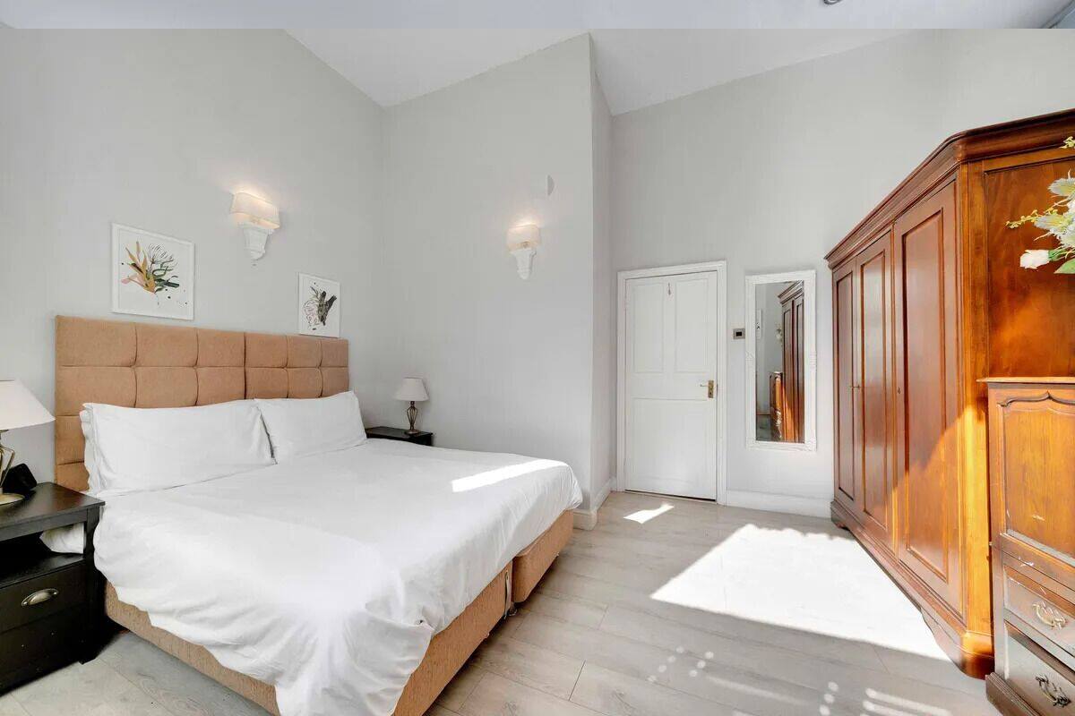A bedroom with a large bed, a wooden wardrobe, and two wall-mounted light fixtures.