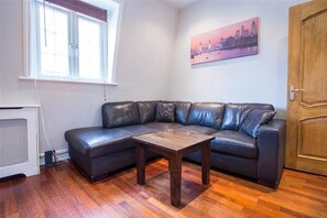 A modern living room with a leather sectional sofa, a wooden coffee table, and hardwood flooring. - Castletown House Apartments (London)