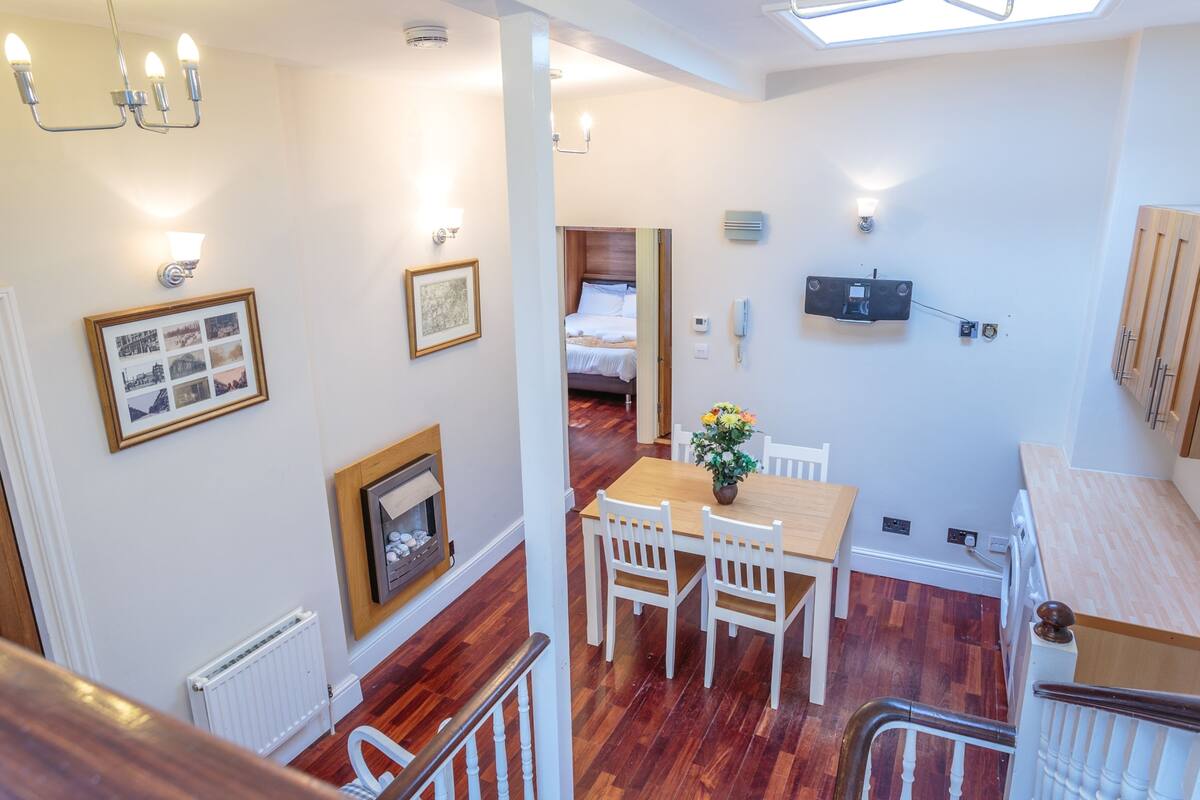 A modern interior with a dining area, a staircase, and a bedroom visible through an open door.