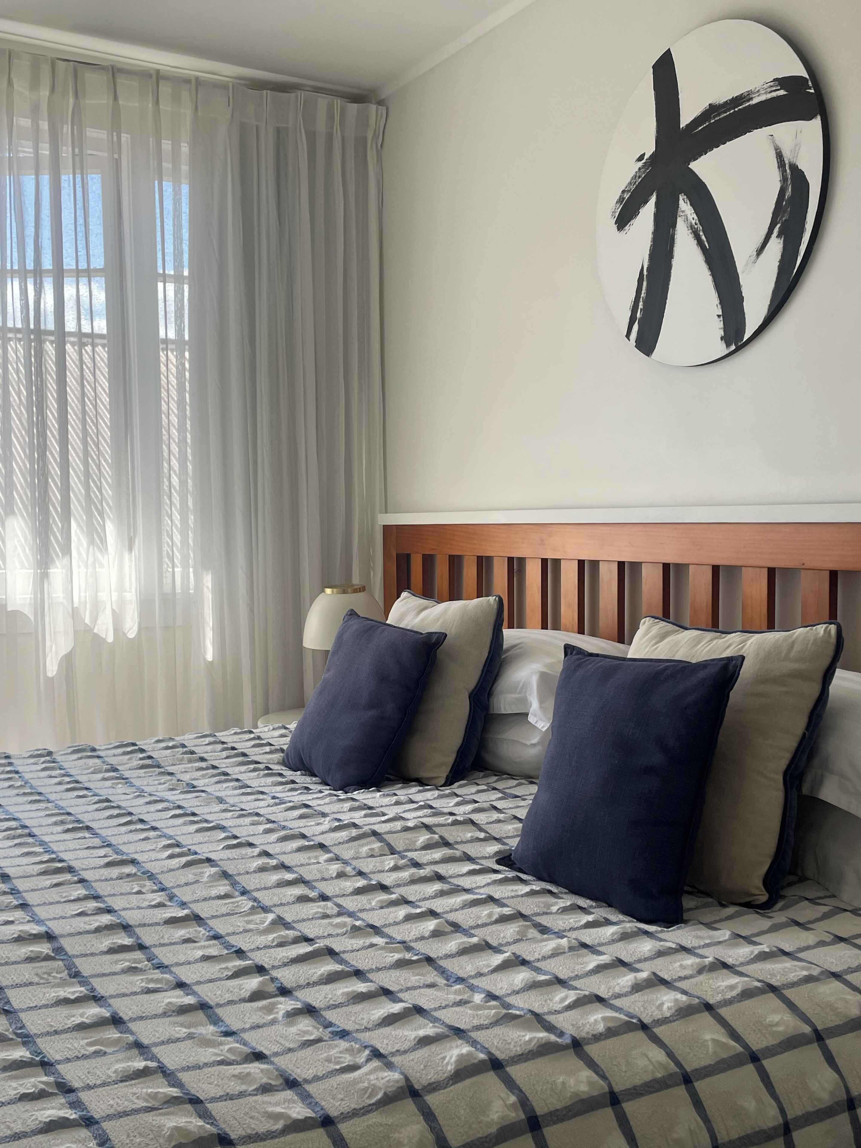 A neatly made bed with a checkered bedspread, a wooden headboard, and several pillows.